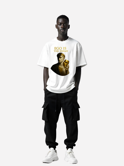 Schwarzer Mann trägt weißes Oversized T-Shirt mit gold-schwarzem Print und Text Ego Is The Enemy, kombiniert mit schwarzer Cargo-Hose und weißen Sneakern
