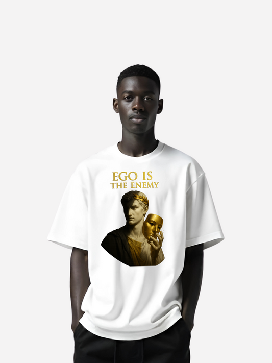 Schwarzer Mann trägt weißes Oversized T-Shirt mit gold-schwarzem Aufdruck "Ego is the Enemy"