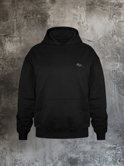Schwarzer Hoodie mit dezentem goldenen Rosenstick auf der linken Brust, fotografiert vor rauer Betonwand. Minimalistisches Streetwear-Design mit Fronttasche und Kapuze, zeitlos und edel.