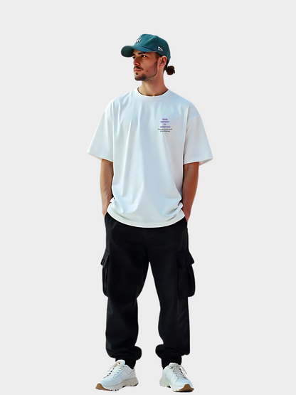 Oversized T-Shirt in Weiß mit Evolution-Print auf der Vorderseite, getragen von einem Model mit grüner Cap, schwarzer Cargohose und weißen Sneakern. Der Brustprint zeigt den Text „FROM INSTINCT TO INTENTION“ in Violett mit dem Zusatz „Evolution ist kein Ende. Sie ist eine Richtung.“ Minimalistisches Streetwear-Shirt mit Message.