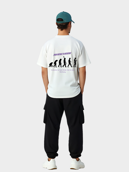 Oversized T-Shirt in Weiß mit Evolution-Grafik auf der Rückseite, getragen von einem Model mit grüner Cap, schwarzer Cargohose und weißen Sneakern. Das Rückendesign zeigt die Silhouette der Evolution vom Affen zum Menschen mit dem Schriftzug „FROM INSTINCT TO INTENTION“ in Violett und dem Zusatz „Evolution ist kein Ende. Sie ist eine Richtung.“