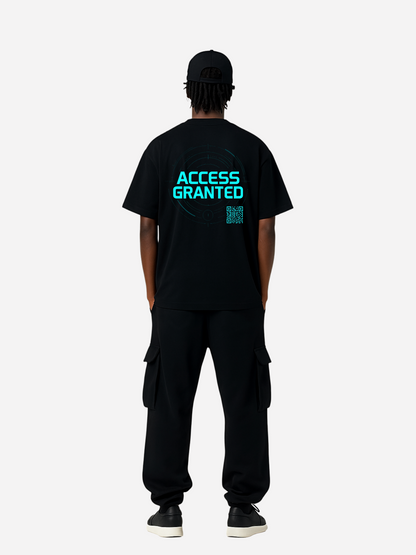 Mockup eines schwarzen T-Shirts in voller Länge am Model mit Rückenaufdruck. Auf der Rückseite leuchtet in Cyan der Schriftzug „ACCESS GRANTED“ mit futurischem Fadenkreuz-Hologramm und kleinem QR-Code. Modernes Cyber-Streetwear-Design.