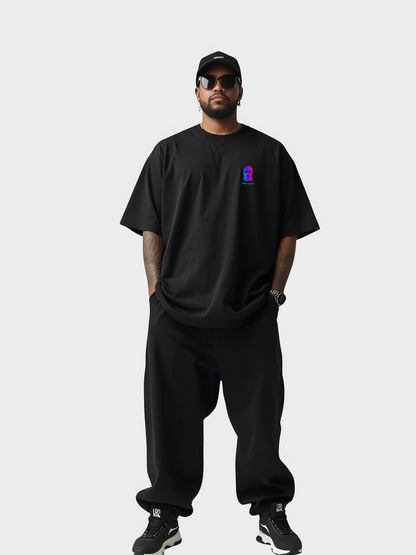 Vyfinity City Noise T-Shirt in Schwarz, Oversized Fit, getragen von einem Model in kompletter Streetwear-Ansicht. Schwarze Cap, Sonnenbrille, weite Hose und Sneaker. Brustprint mit bunter Maske im VHS-Style.