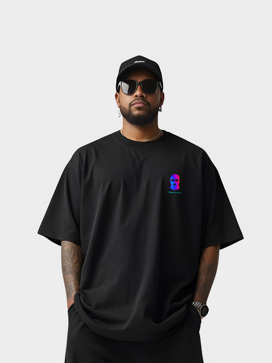 Vyfinity City Noise T-Shirt in Schwarz, Oversized Look, getragen von einem Model mit Cap und Sonnenbrille. Auf der Vorderseite dezentes kleines Logo mit bunter Maske auf der Brust.
