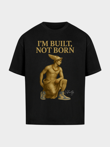 Schwarzes Oversize T-Shirt mit goldener Statue im antiken Look, kombiniert mit modernen Sneakers. Oben goldener Schriftzug „I’M BUILT, NOT BORN“ – urbaner Streetwear-Style mit starkem Motivations-Statement.