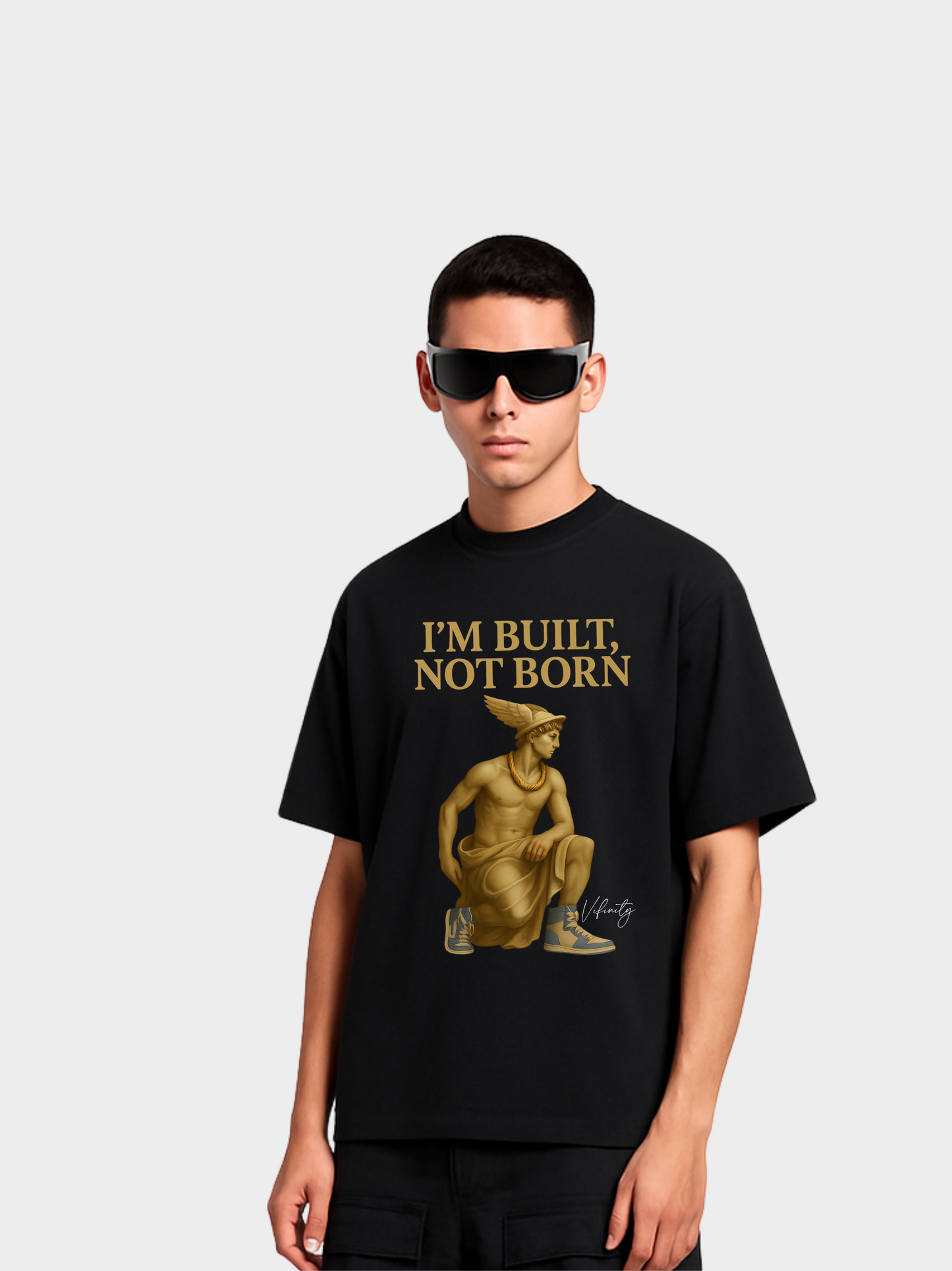 Schwarzes Oversize T-Shirt mit goldener Aufschrift „I’m built, not born“. Design zeigt eine antike Statue in moderner Pose mit Sneakers – Symbol für Stärke, Disziplin und Selbstaufbau. Urban Streetwear mit tiefer Botschaft und künstlerischem Look.