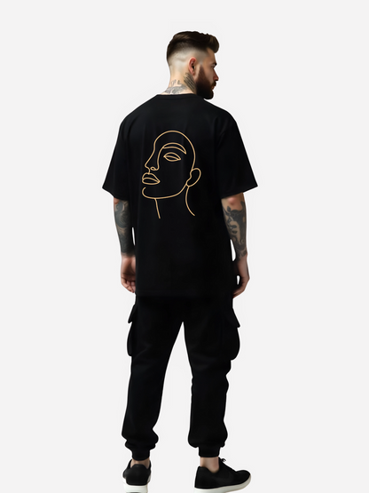 Vyfinity Oversize T-Shirt in Schwarz mit großem Line-Art Gesicht auf dem Rücken, getragen von tätowiertem Model in schwarzer Cargo-Jogginghose und Sneakers. Streetwear Outfit in Rückenansicht.