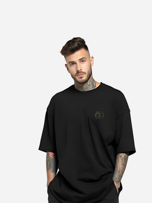 Vyfinity Oversize T-Shirt in Schwarz, getragen von einem tätowierten Model. Minimalistisches Line-Art Gesichtsmotiv auf der Brust, moderner Streetwear-Look mit lockerem Schnitt.