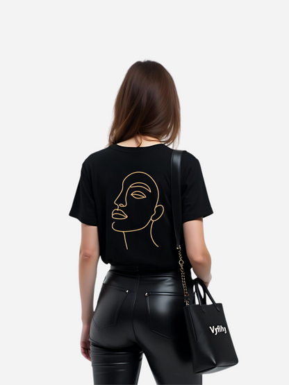 Vyfinity Oversize T-Shirt in Schwarz mit großem Line-Art Gesicht-Print auf der Rückseite, kombiniert mit schwarzer Lederhose und stylischer Vyfinity Bag. Moderner Damen Streetwear Look im urbanen Style.