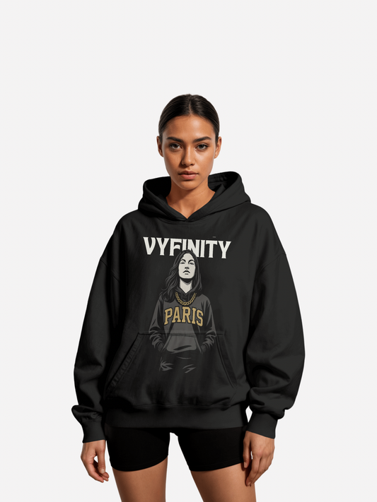 Frau trägt schwarzen Vyfinity Hoodie mit Illustration einer Frau, goldener Kette und Aufdruck „PARIS“ in goldenen Buchstaben