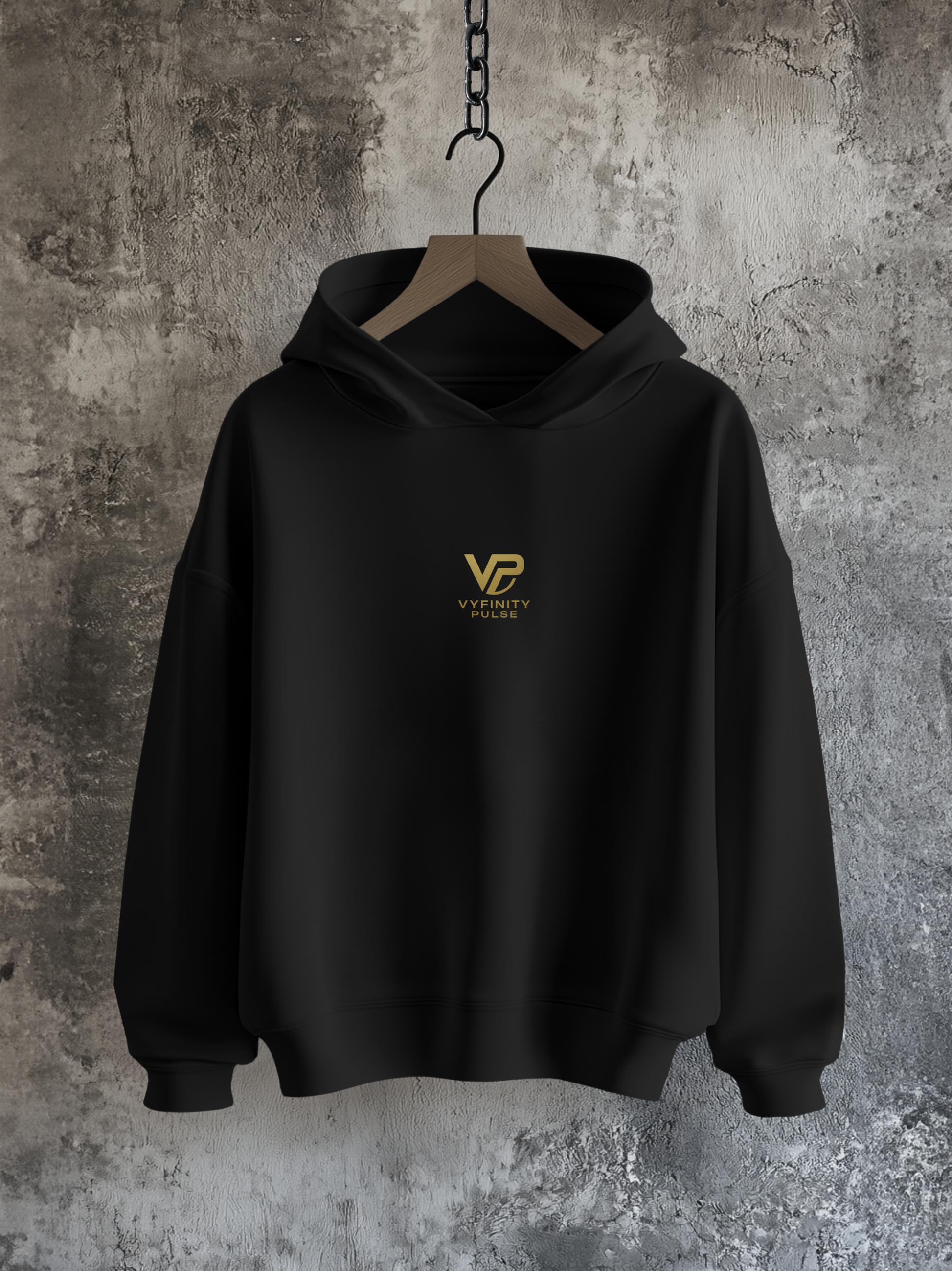 Vyfinity Pulse Hoodie in Schwarz – Frontansicht mit goldener VP-Stickerei, präsentiert am Holzbügel vor rustikalem Betonhintergrund
