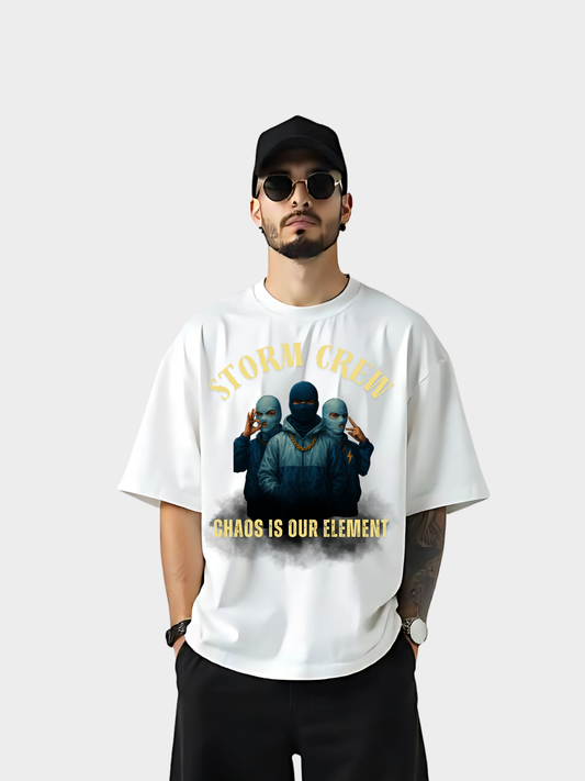 Vyfinity Storm Crew T-Shirt in Weiß, Frontansicht getragen von einem Model mit schwarzer Cap und Sonnenbrille. Aufdruck mit drei maskierten Figuren, goldener Schriftzug „Storm Crew“ oben und „Chaos is our element“ unten.